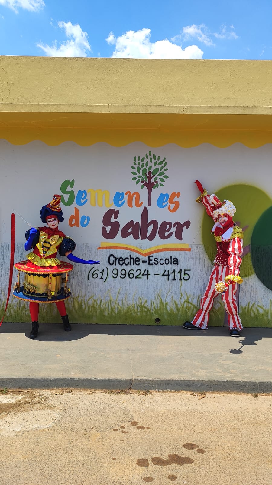 Fachada da Sementes do Saber com o logo, o telefone e personagens recebendo as crianças